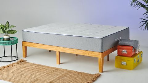 The Nectar Mattress placed on a light wooden bed frame with an orange metal suitcase at the end