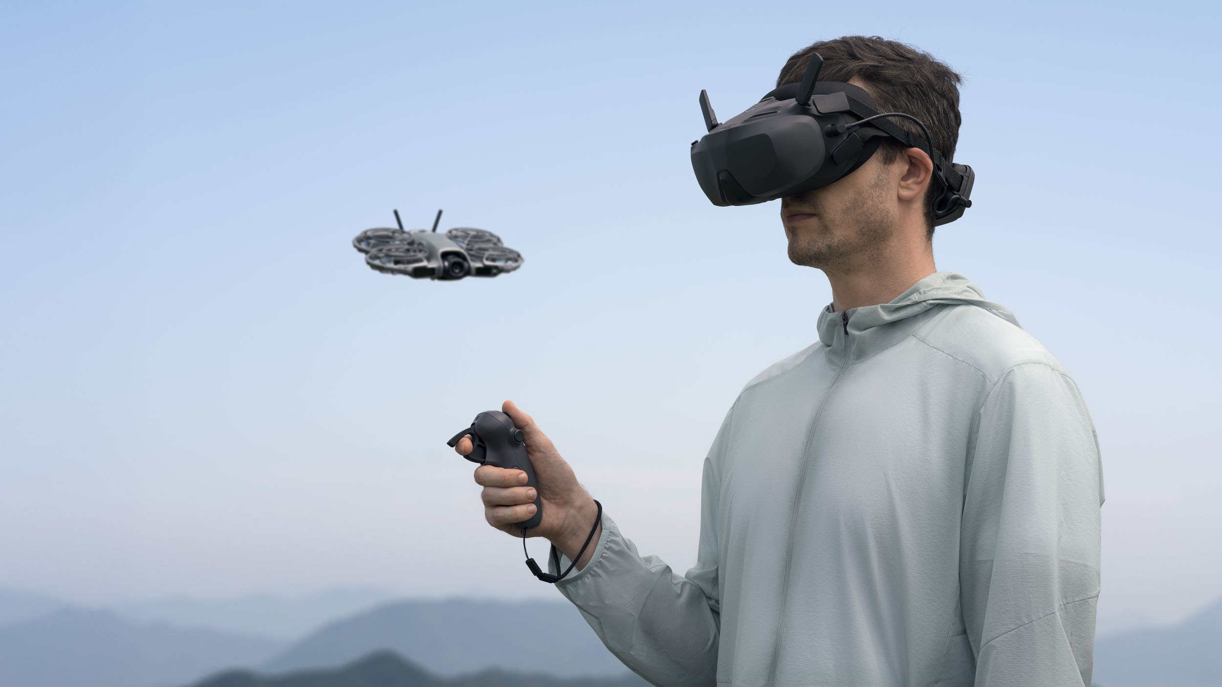 DJI Neo 2 selfie drone in flight alongside man wearing DJI goggles and holding a controller