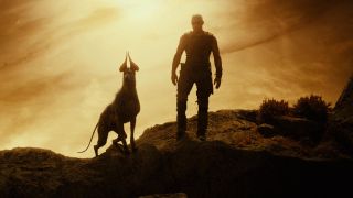 Still from the movie series The Chronicles of Riddick. Here we see Riddick (bald man with dark goggles) standing with a large dog-like creature which has big, pointed ears.