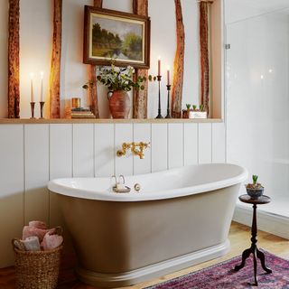 a bathroom with freestanding bathtub and shelf with lit candles a job vase with flowers and some books