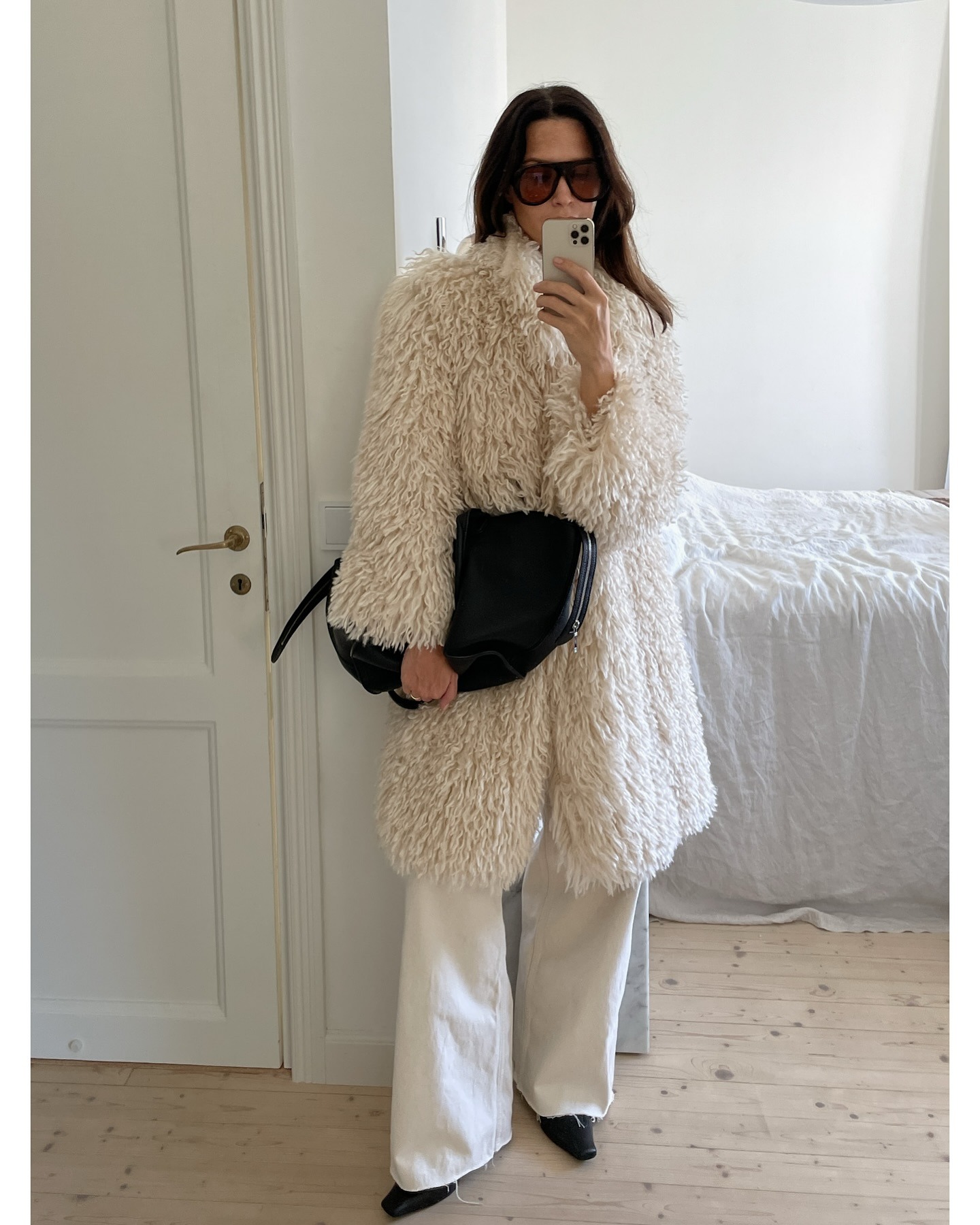Woman wearing white jeans with furry coat, black bag, and pointed boots.