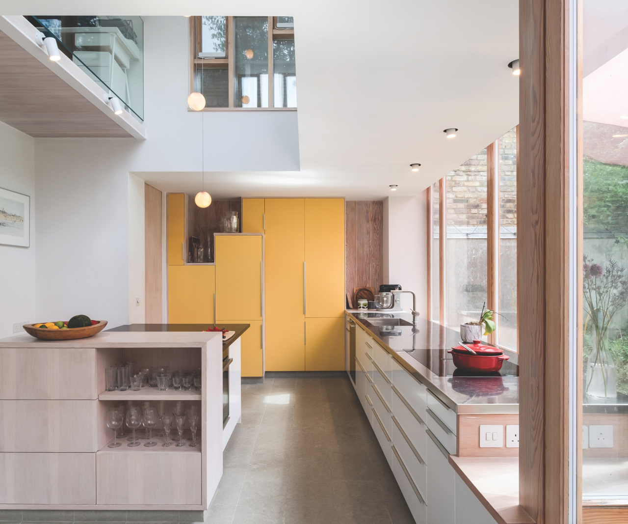Kitchen with orange cabinets at the far end, an island with exposed glasses and large windows on the right hand side overlooking the garden