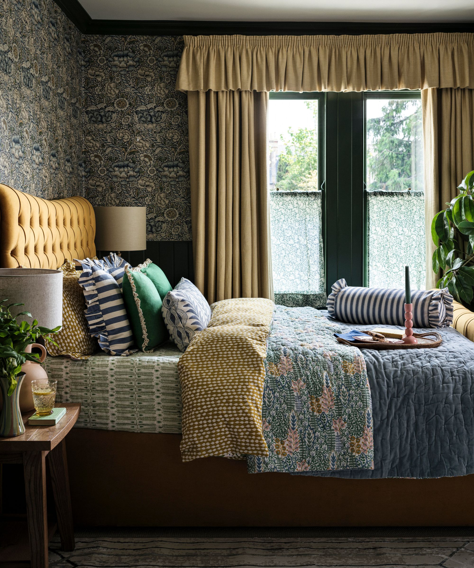cottagecore maximalist wallpapered bedroom with yellow ruffle top curtains, yellow bed, floral bedding and striped ruffled pillows