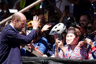 Prince William waving to a crowd of fans including one wearing a Prince William mask