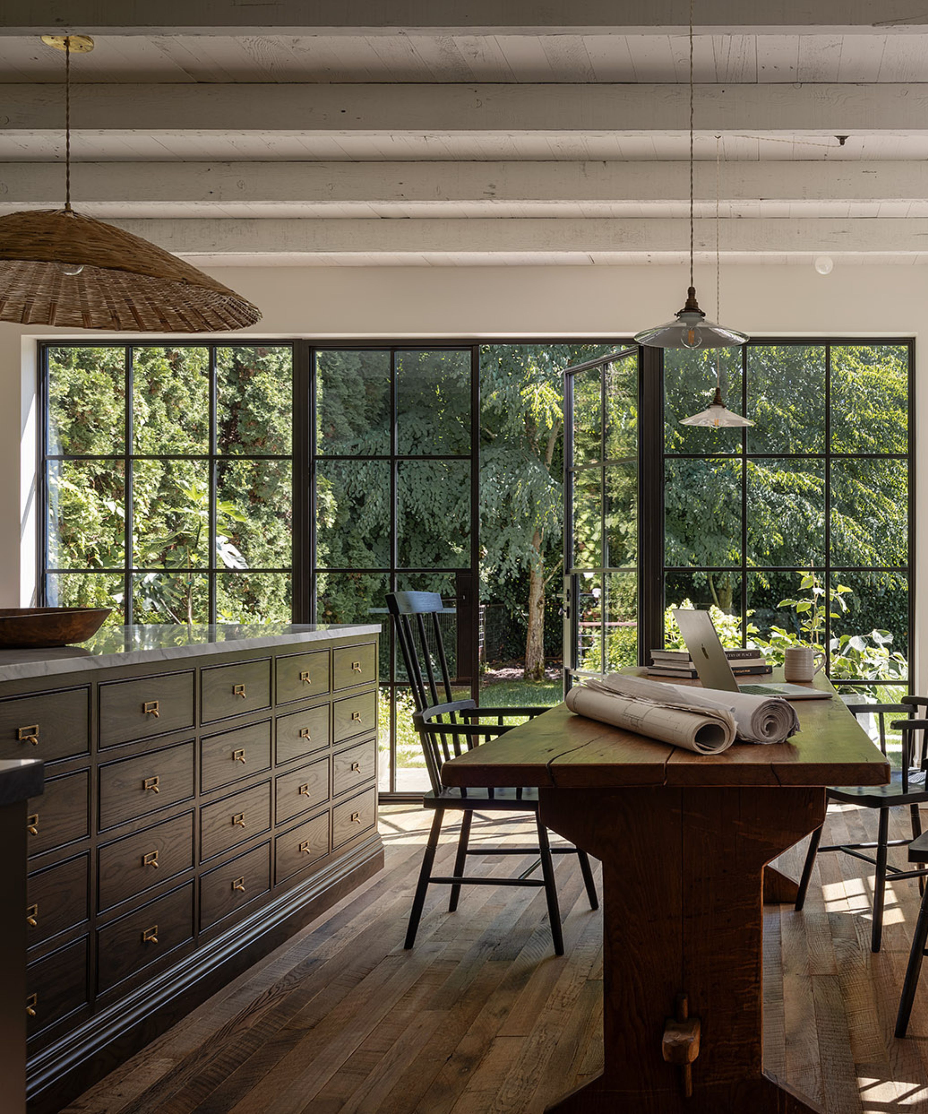 a garage DADU conversion transformed with large glass and steel doors with a view to the backyard, a large dark wooden kitchen island and a rustic farmhouse table with antique chairs