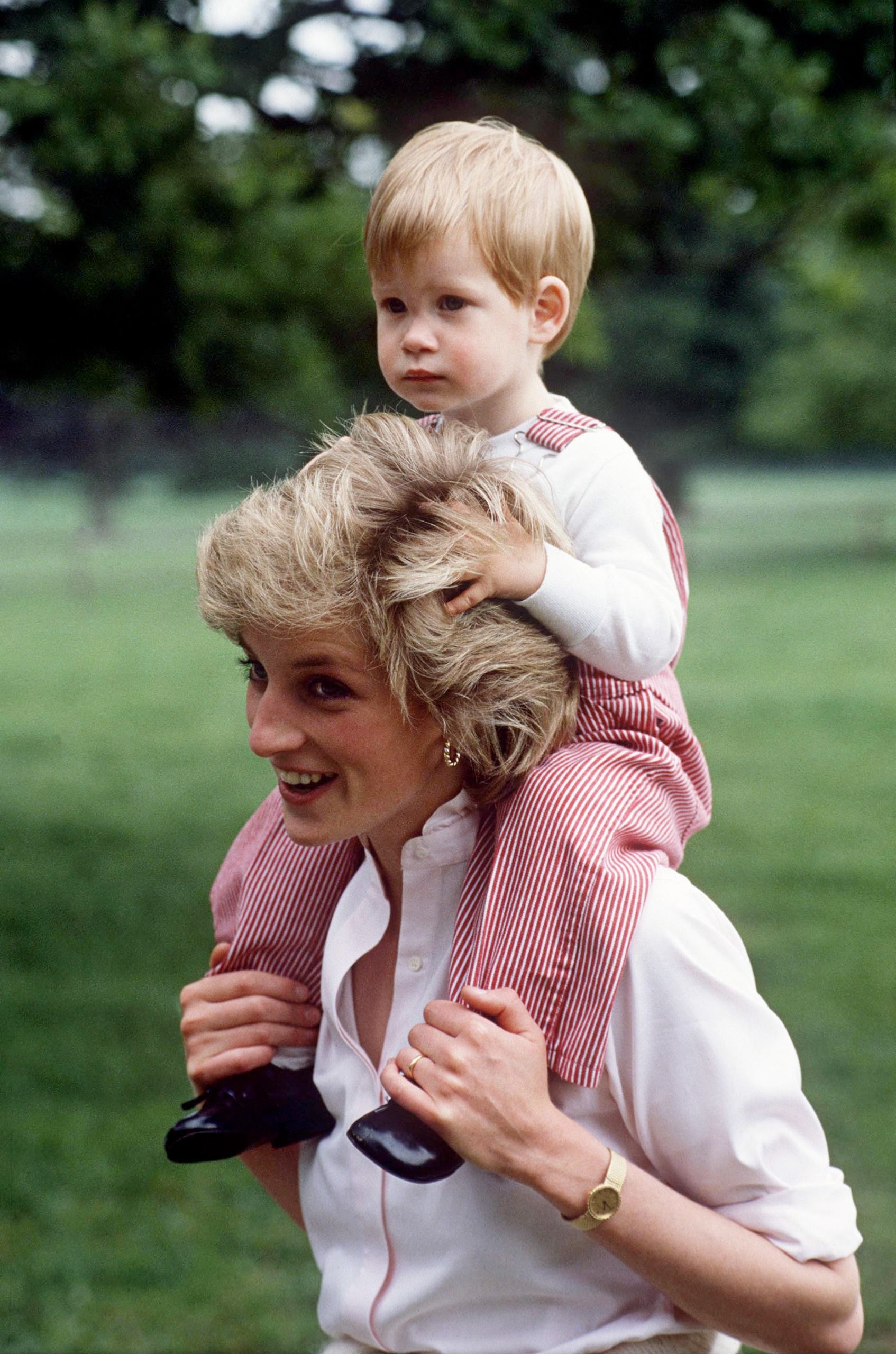 Prince Harry, dressed in striped overalls, gets a piggyback ride from Princess Diana in 1986