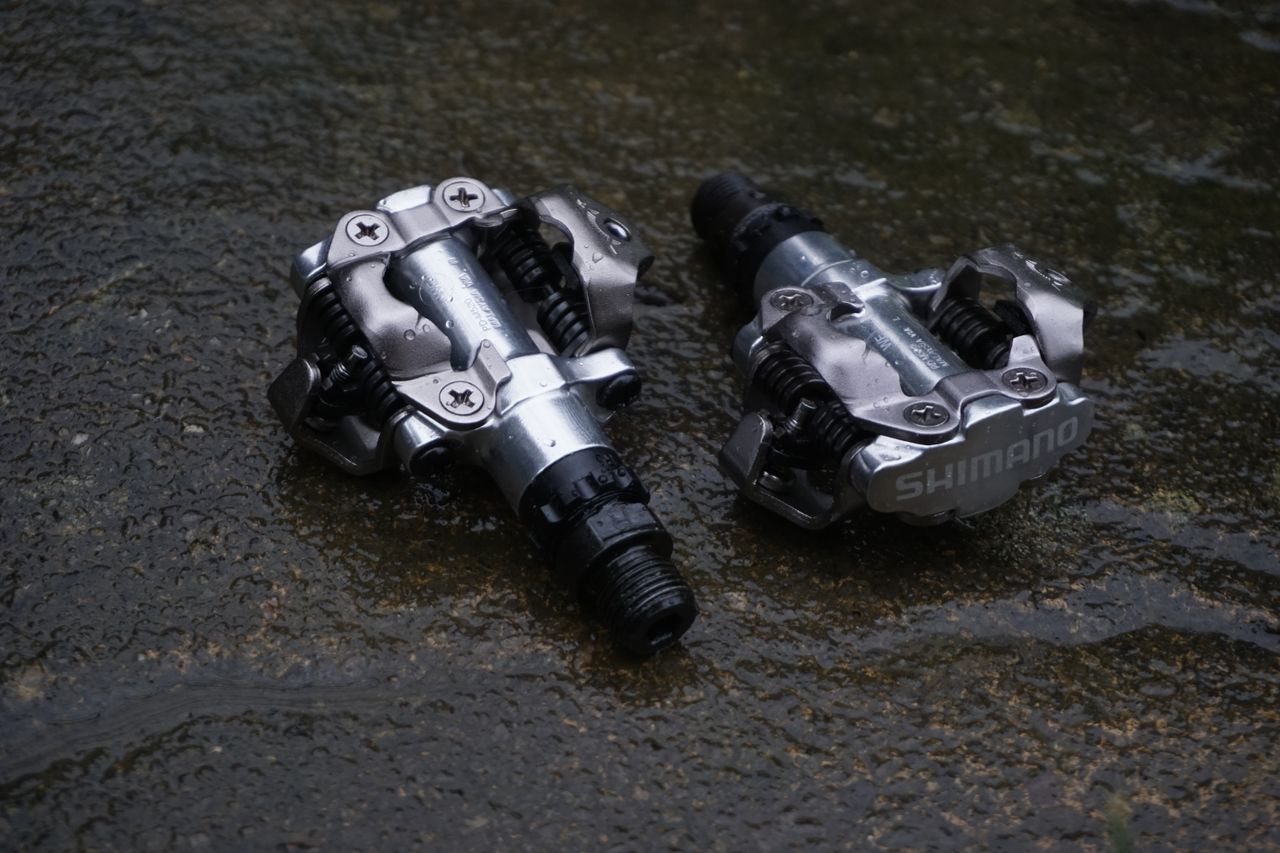 A pair of silver gravel bike pedals on a stone surface