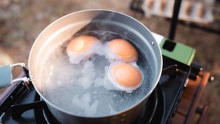 Three eggs in a pan of water on a camping stove