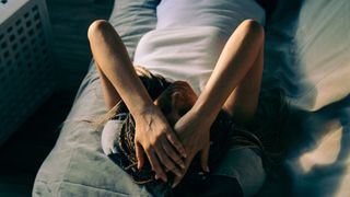 Woman with head in hands with hangover, lying on sofa