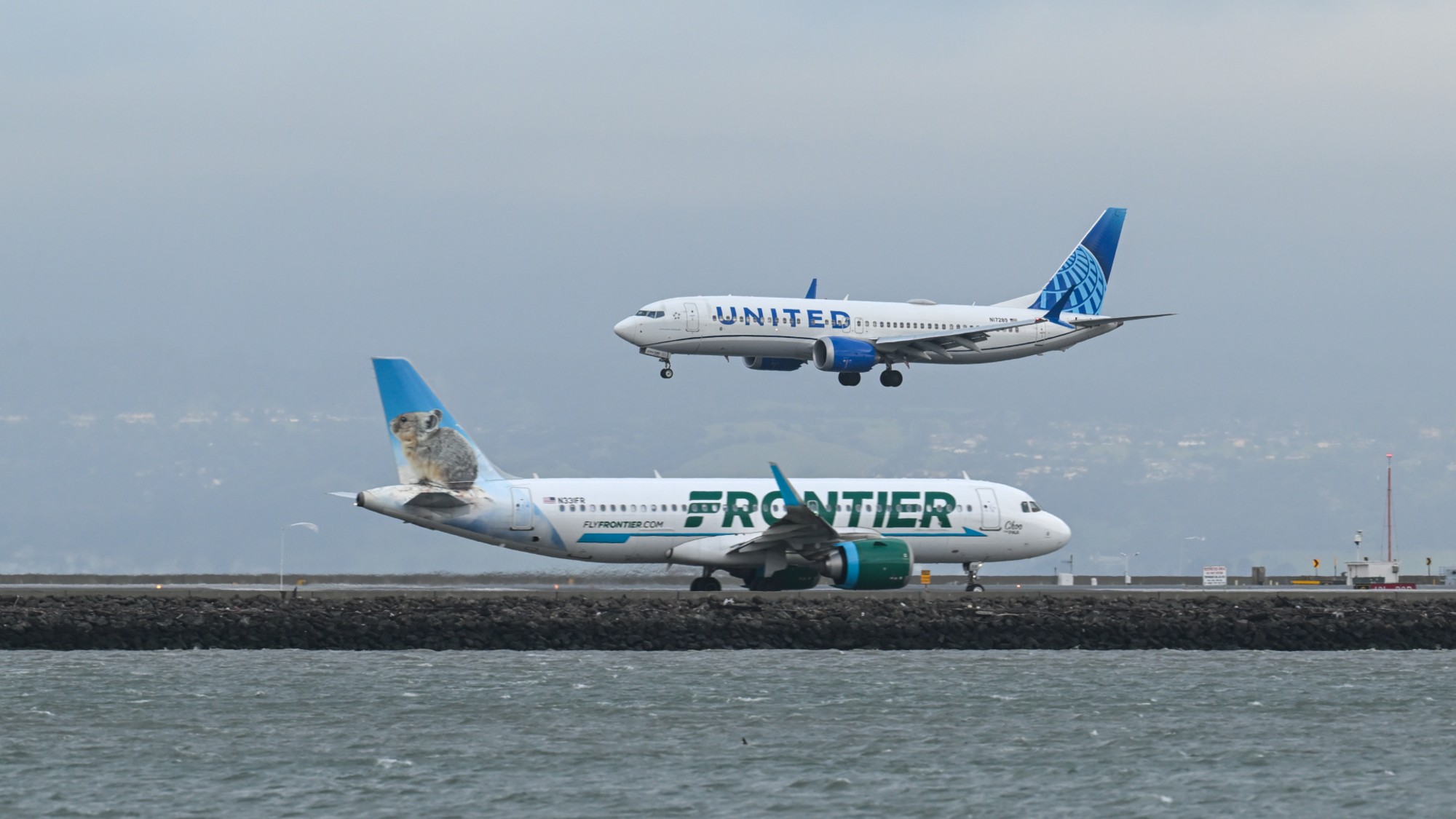 A Frontier flight prepares to take off as a United flight lands nearby at San Francisco International Airport on March 17, 2025.