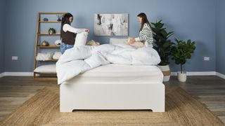 Two women stand either side of a mattress in a bedroom, placing the covers on a duvet