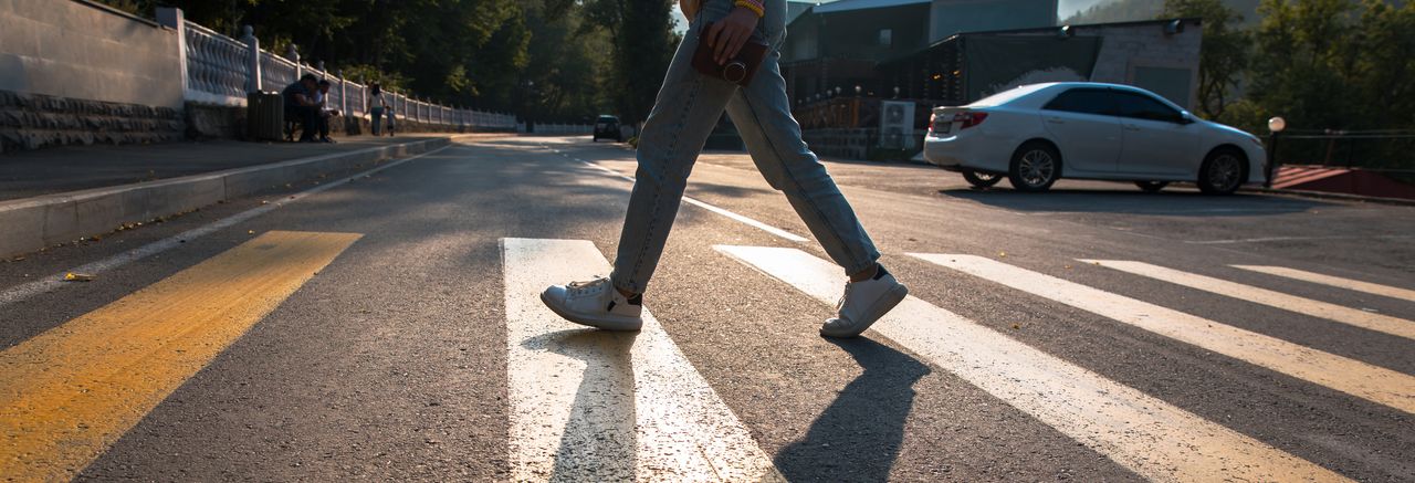 Person crossing crosswalk at sunset with car in background