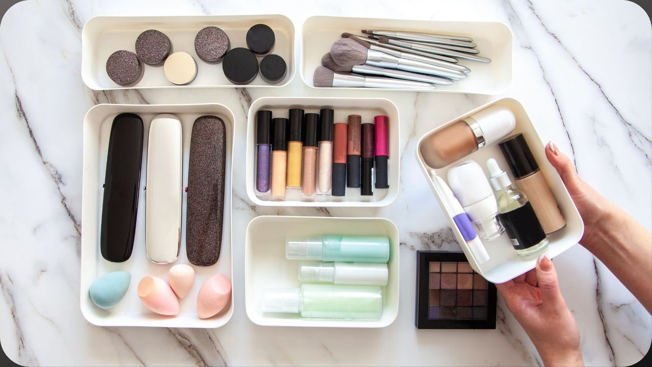 A selection of makeup that&#039;s been decluttered into acrylic storage with a woman&#039;s hand