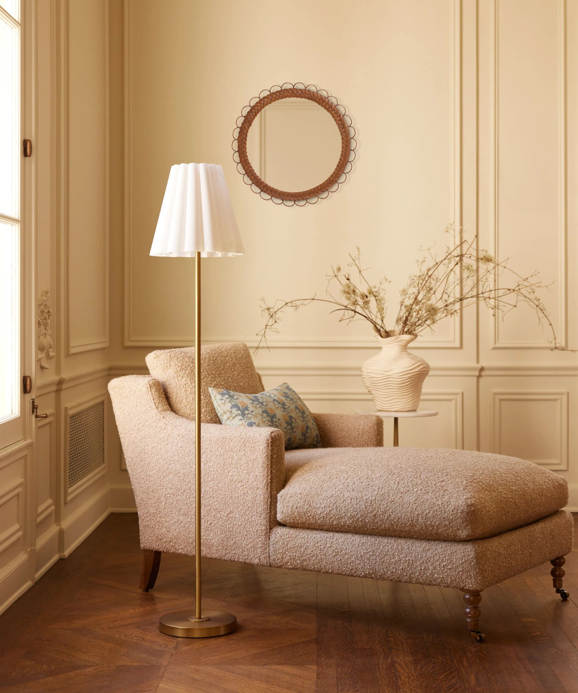 Chaise lounge on wooden floor with a scalloped floor lamp and rattan mirror hung on the panelled wall plus a side table and plant