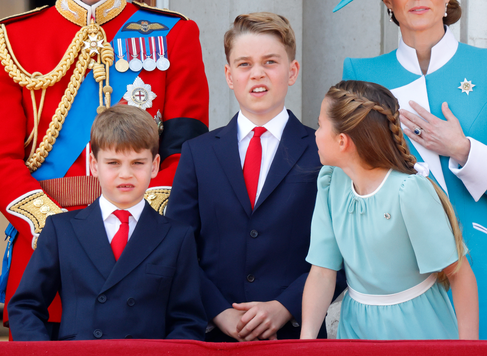 Prince Louis wears a navy suit, white shirt, and red tie at Trooping the Colour 2025