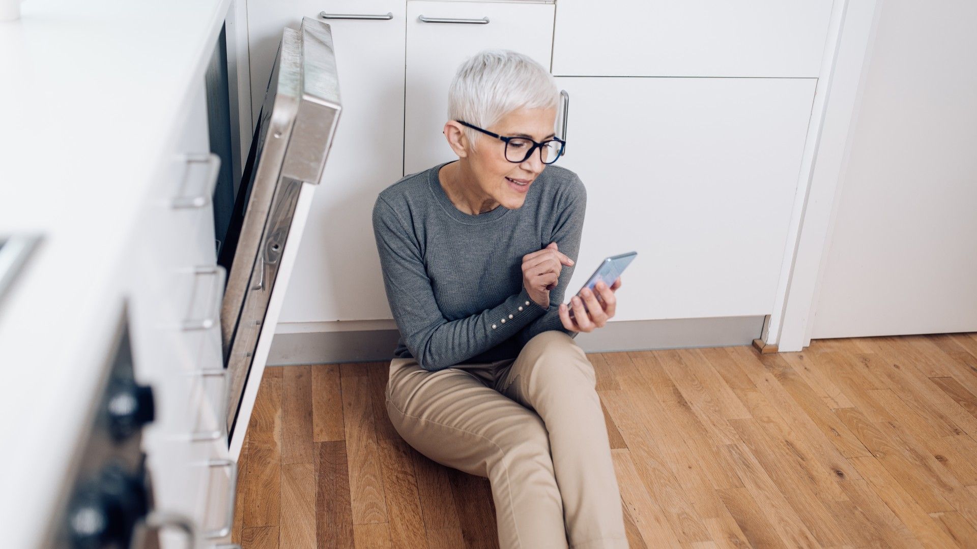 person reading instruction manual sitting beside a dishwasher in the kitchen