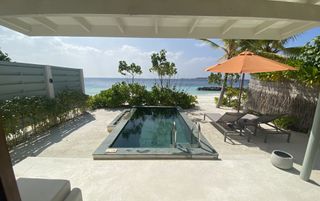 A private plunge pool surrounded by sand looking out over green shrubbery to the ocean