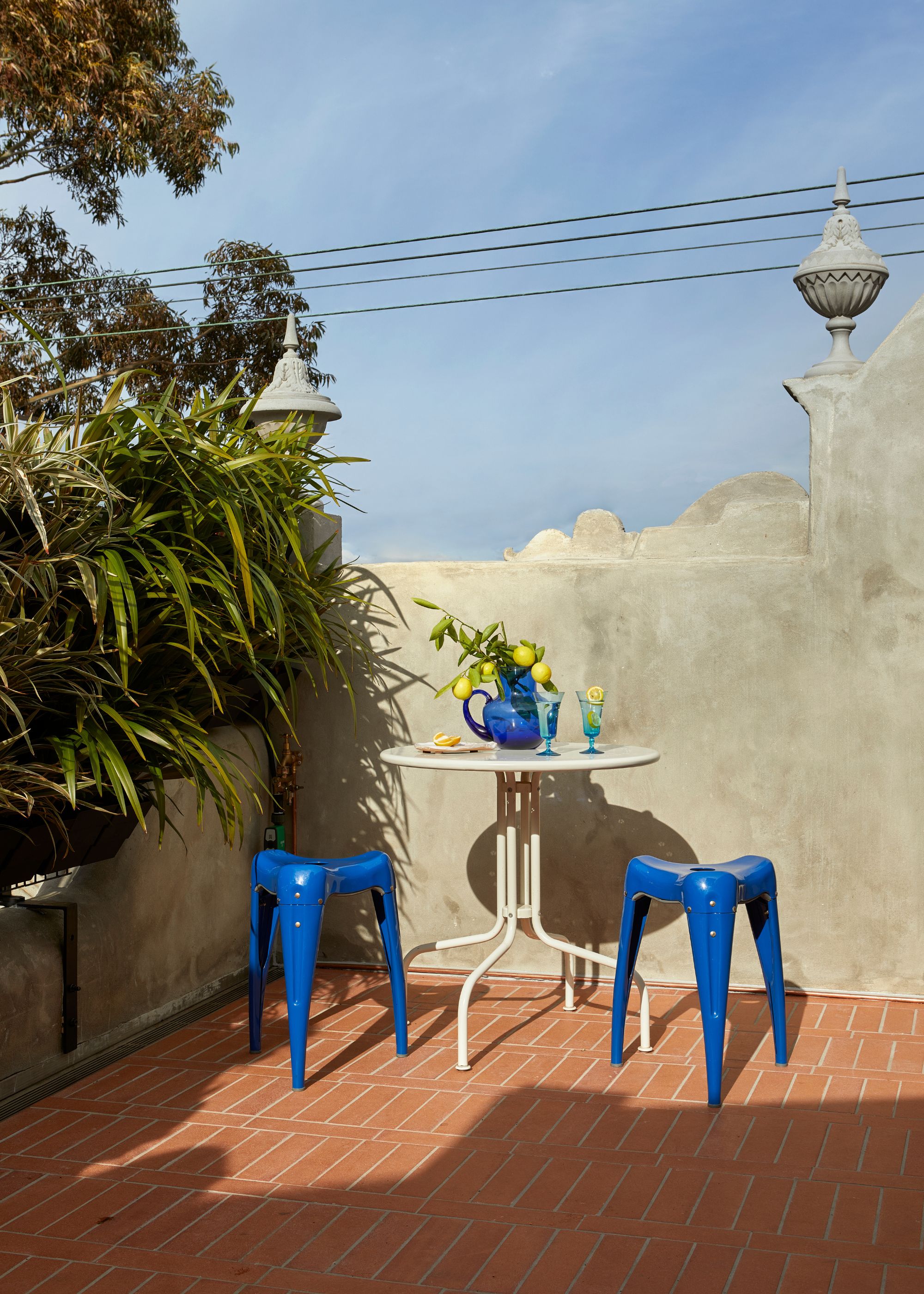 A terrace garden with a brick floor, cement walls, and a white bistro table with cobalt blue stools
