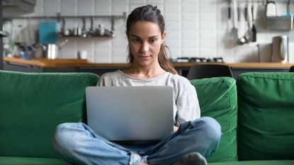 A woman sitting on a couch cross-legged and using a laptop