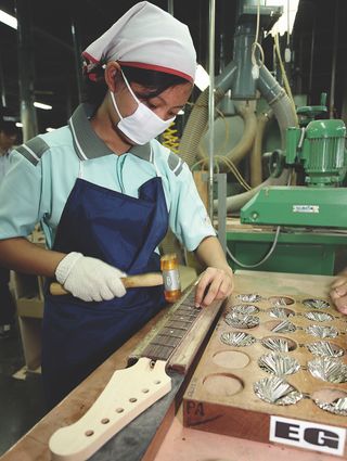 A woman at the Yamaha guitar factory hammering frets into the fretboard of an electric guitar