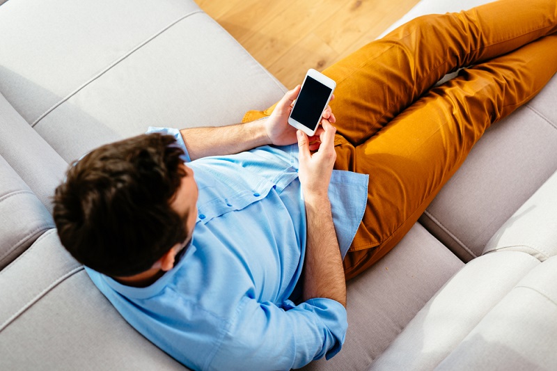 A man sitting on a couch holding a smartphone.