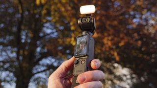 DJI Osmo Pocket 4 vlogging camera with natural background at golden hour, and the user in the frame of the screen