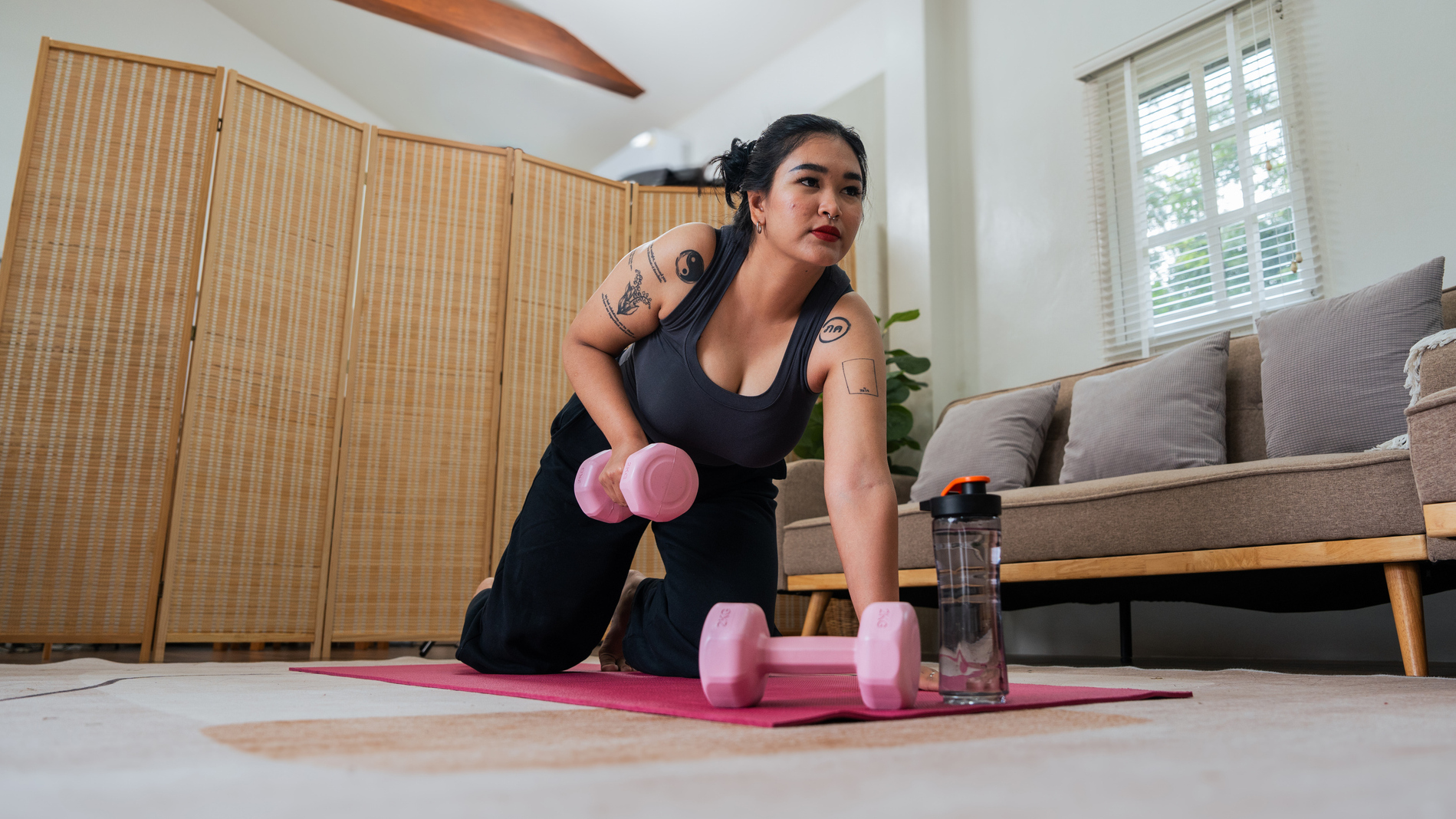 Woman on all fours lifting dumbbell from the floor. She is in a domestic setting.