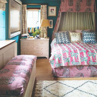 A maximalist bedroom painted in bright blue with pink and blue-printed bed and bed linen