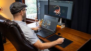 3D artist using Wacom Intuos Pro (2025) with a desktop setup on a wooden desk