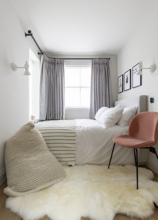 small white bedroom with gray drapes, white wall lights, sheepskin rug, orange chair, knitted beanbag, artwork