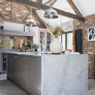 kitchen area with beams and exposed brick wall and marble worktop