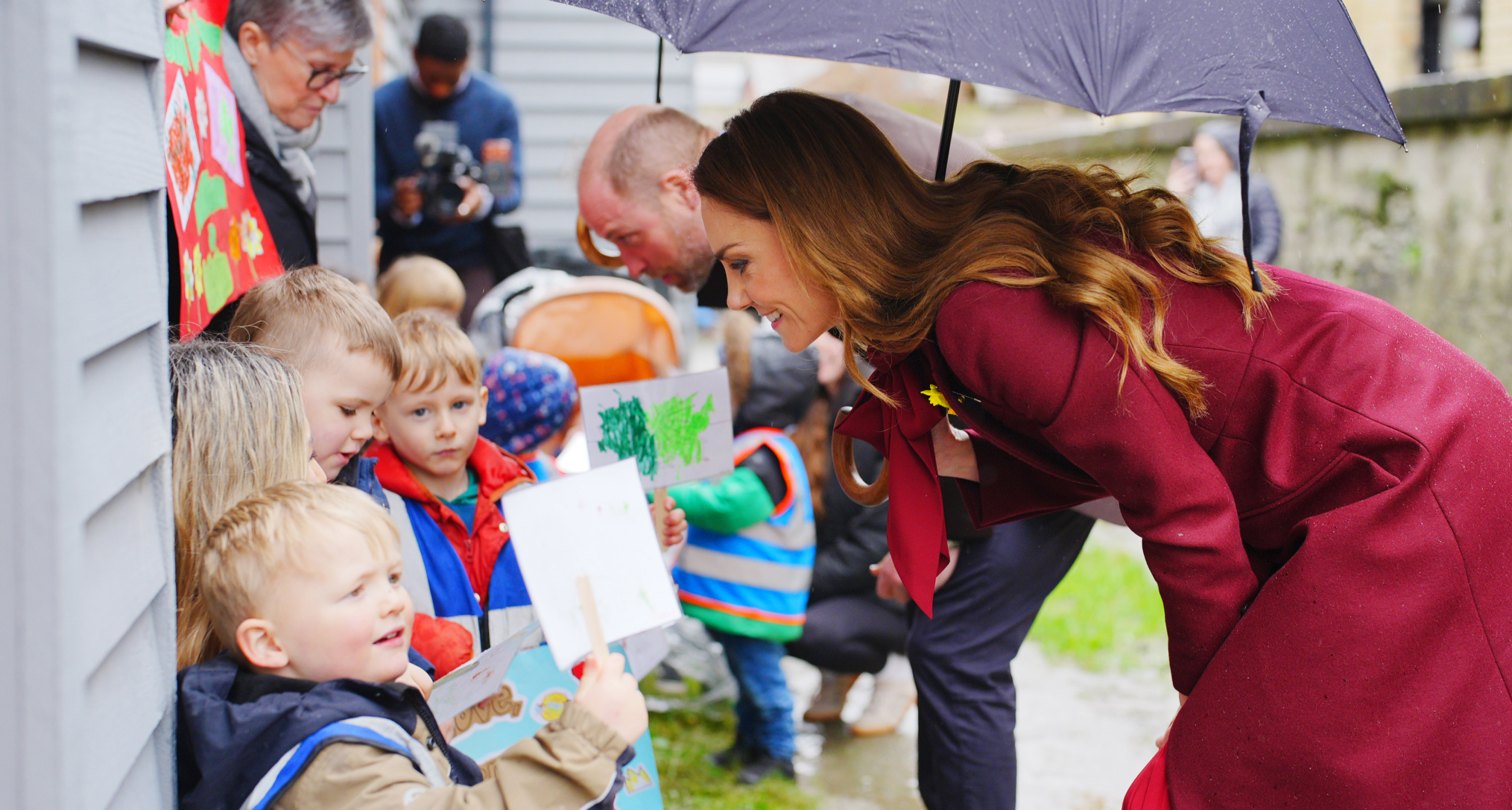 Princess Kate talking to kids bending over holding an umbrella