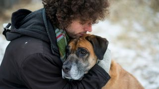 Owner hugging dog in the snow outside