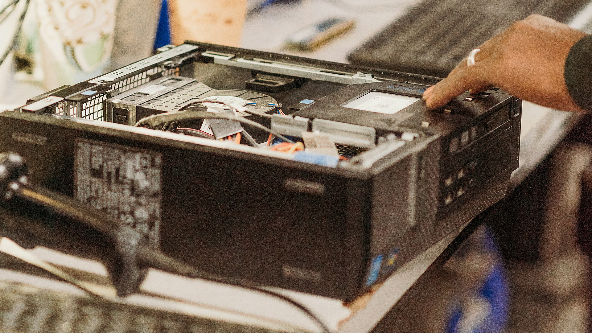 A desktop tower on a desk with its cover taken off and a hand on top of it