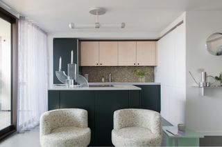 Small kitchen with cabinetry in two colours, pendant light above breakfast bar and two armchairs in front of kitchen