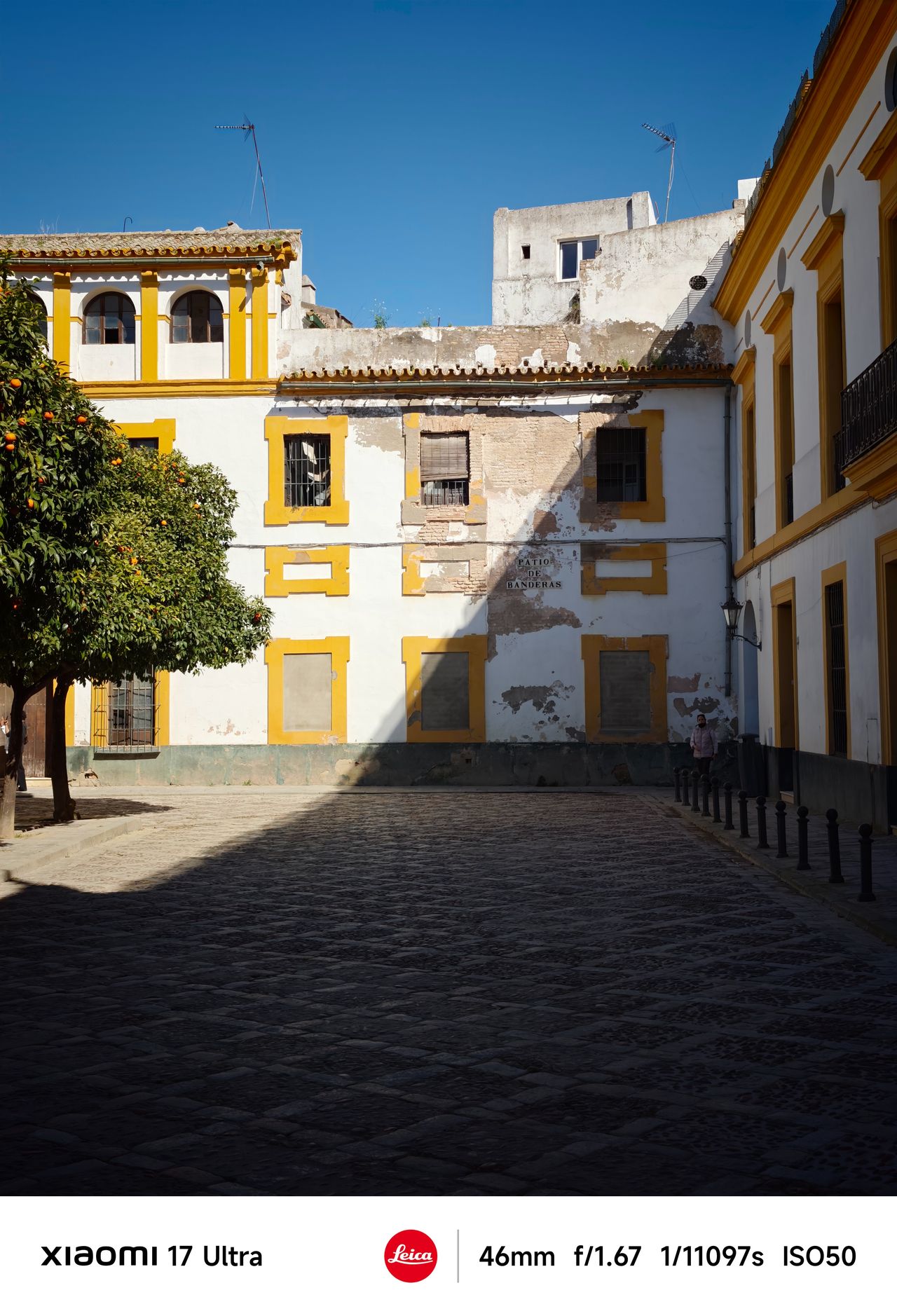 Sunlit courtyard with weathered white-and-yellow buildings and long shadows across cobblestones.