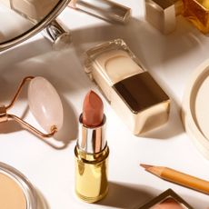 A selection of make-up, beauty tools and a candle laid out on a white surface 