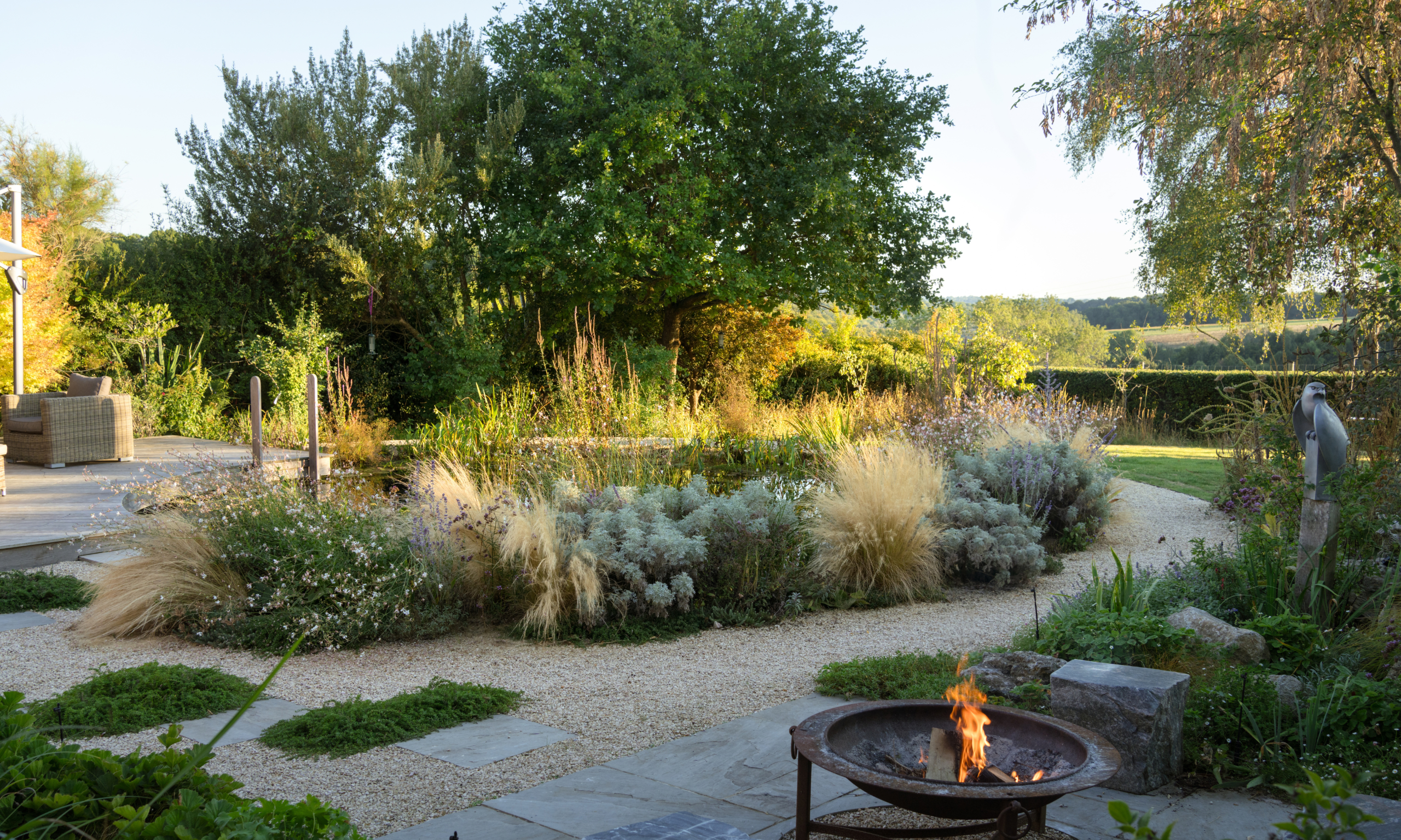 An autumnal garden landscape with gravel paths, fire pit and ornamental grasses at sunset