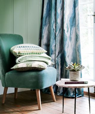 Bedroom corner with velvet chair stacked with cushions and a throw