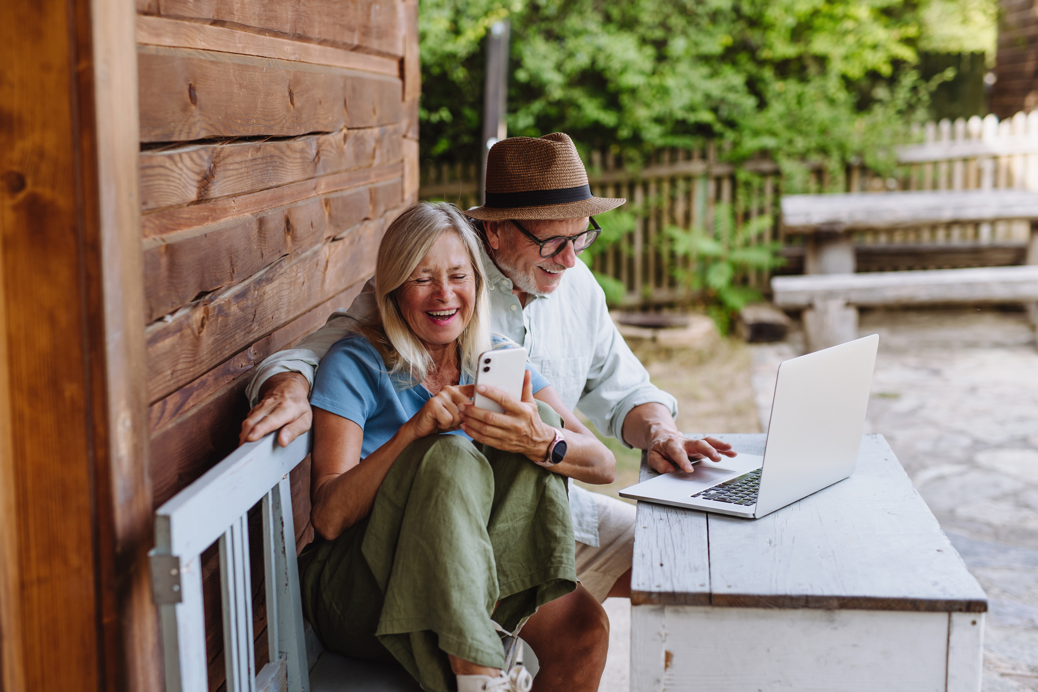 A couple laughing while scrolling social media on their front porch.