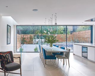 A large kitchen extension with glass sliding doors and a long dining table with blue and cream chairs and flowers