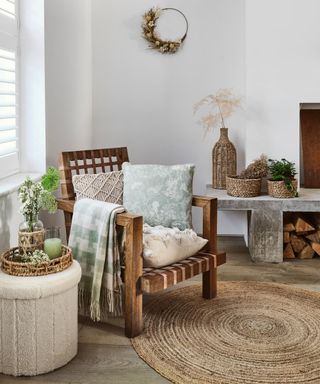 A living room with wooden chair with cream/green soft furnishings, concrete table, and boucle ottoman storage pouffe