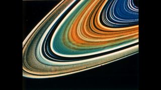 A close-up of a portion of Saturn's ring system showing distinct bands of blue, orange, yellow, and white. 