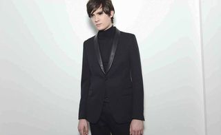 A male model wearing a look from Gucci's collection. He is wearing a black turtle neck jumper and black suit with leather lapels