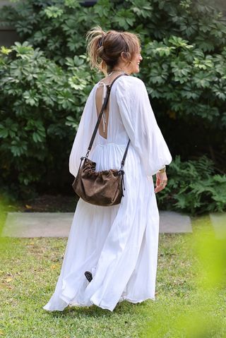 jlo wears a white maxi dress with a brown suede drawstring bag