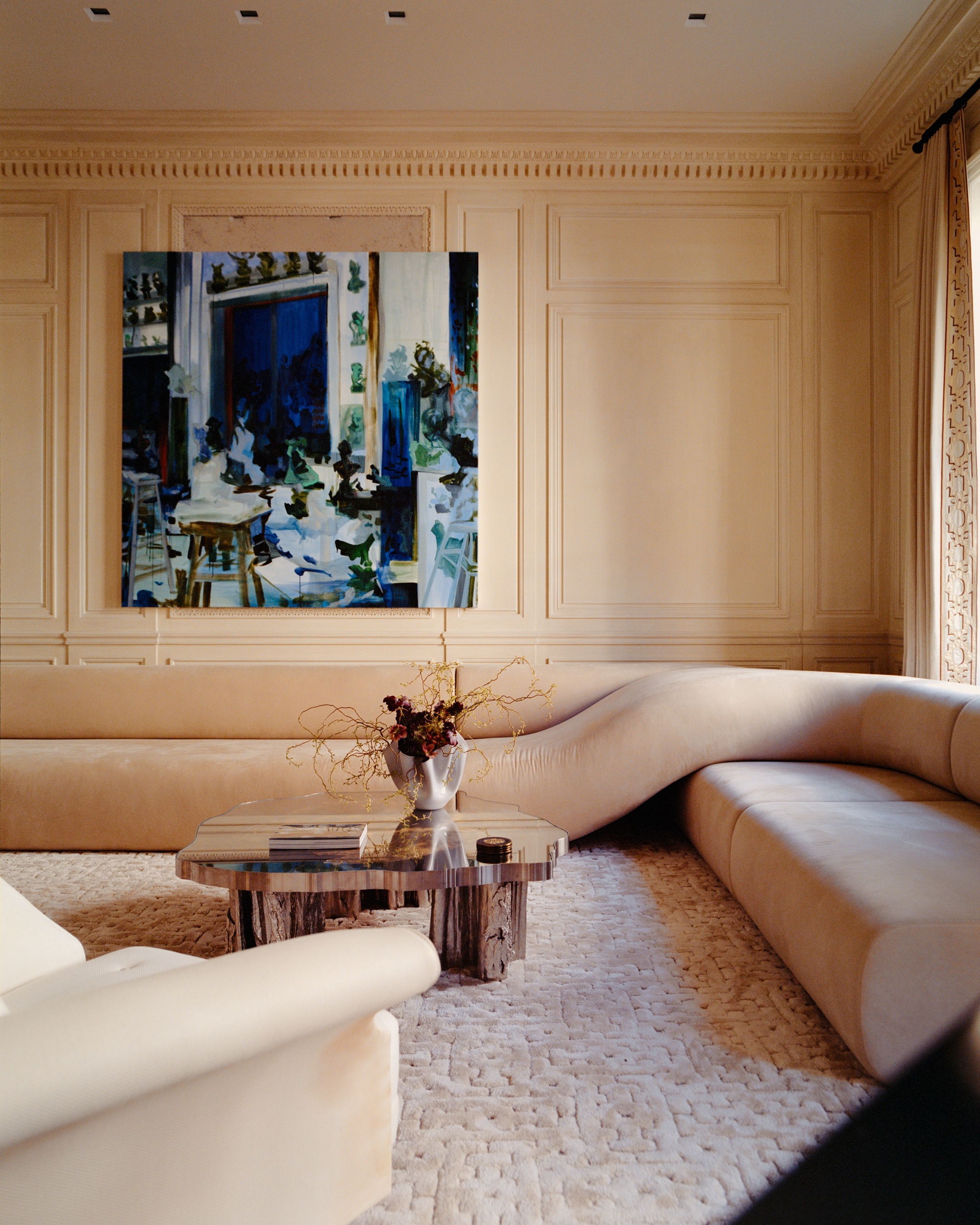a living room with a twisted sofa in a neutral colour, with a rug and neutral walls with painted blue artwork