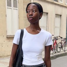 A woman wearing a white T-shirt, gray pencil skirt, and black leather bag