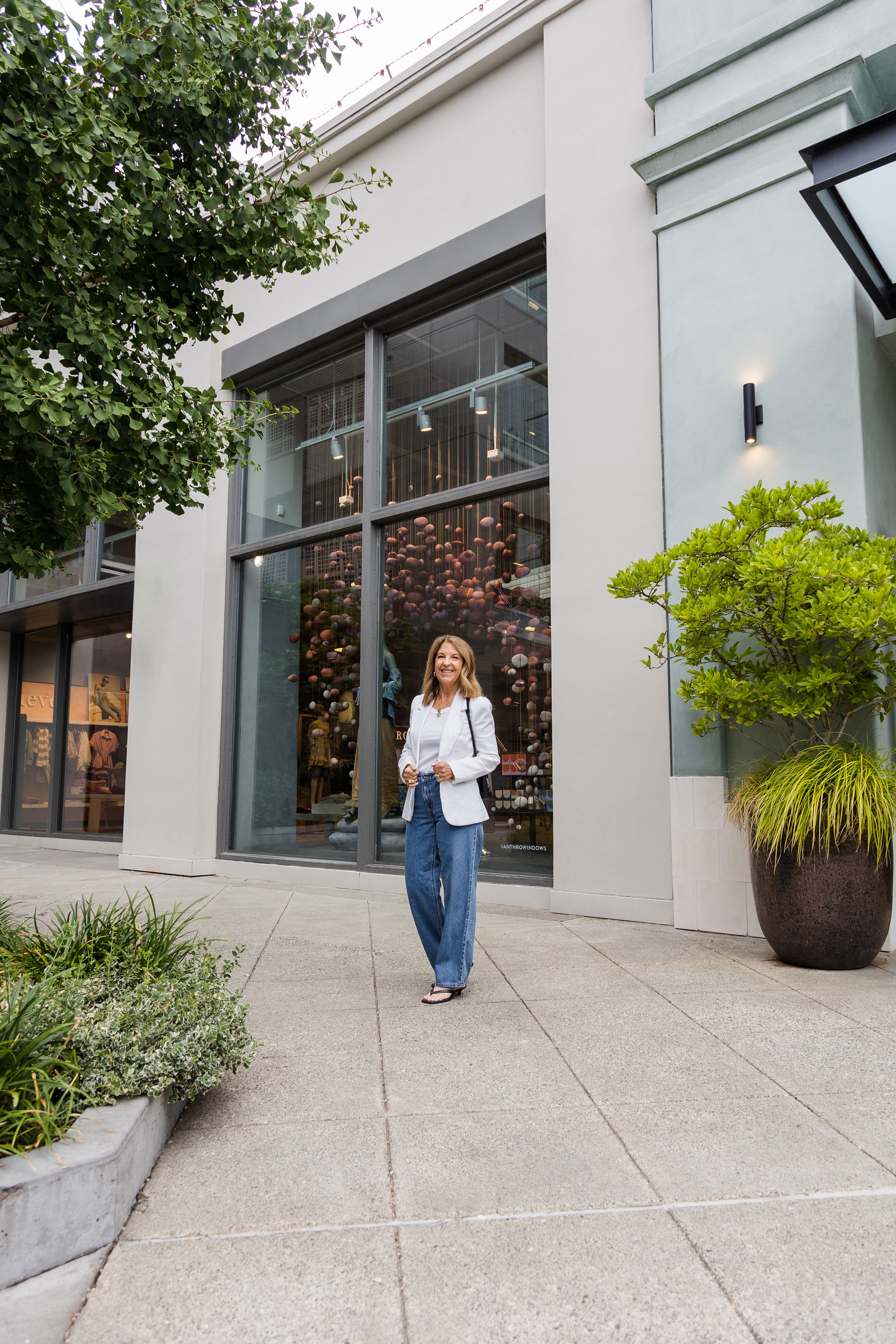 Um estilista Nordstrom usando jeans folgados, uma blusa branca e um blazer branco.