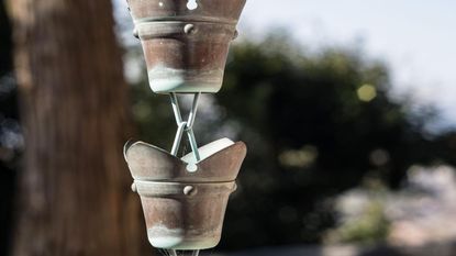 A close up of a rain chain hanging from a roof