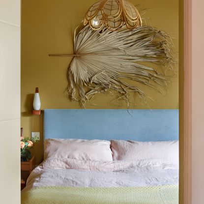 A mustard yellow-painted bedroom with a baby blue headboard and light pink and yellow bedding